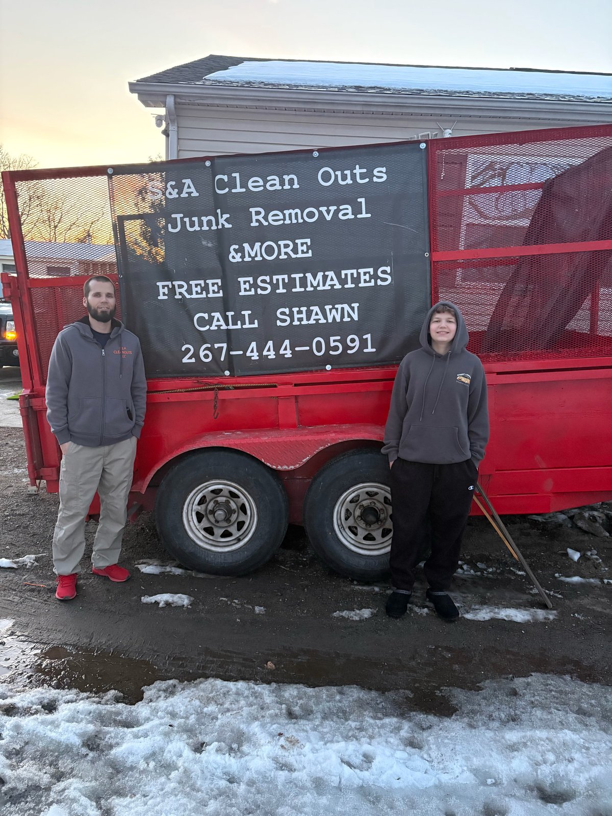 Two S&A Cleanouts crew members standing in front of the red junk removal trailer with the company service sign